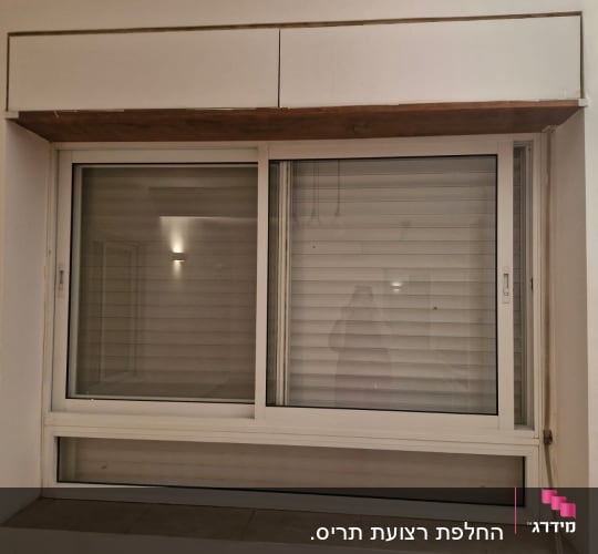 חלון עם תריסים סגורים על קיר לבן